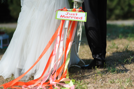 Groom and bride on white bicycle with just married sign and colorful ribbons. Outdoors. Loving couple in the background.の写真素材