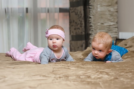 Baby girl lying on belly on bed in bedroom with golden linens. Charming 5-month-old girl and boy...