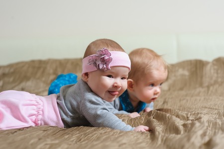 Baby girl lying on belly on bed in bedroom with golden linens. Charming 5-month-old girl and boy smiling and grimacing showing the tongue. Home interior in background.の写真素材