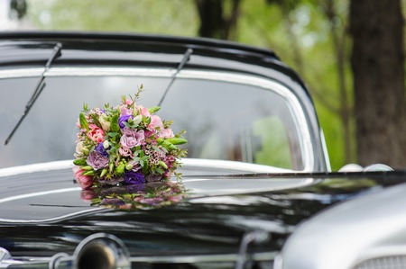 Elegant bridal bouquet of different flowers on the hood of a black retro carの写真素材
