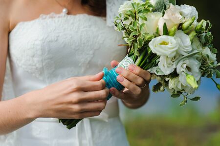 Bride holds a wedding bouquet. Beautiful wedding bouquet tied with white lace and blue ribbon. Outdoors. river in the background. Sunny day.の写真素材