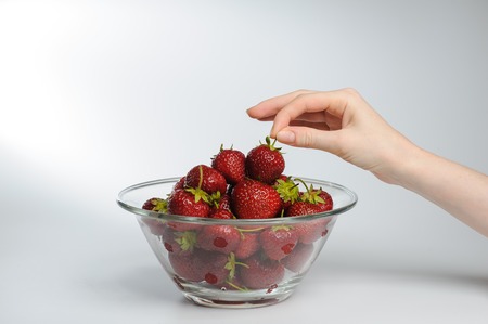 Girl holding strawberries. close-up. Glass Bowl Of Strawberries. Fresh strawberries in hands on white background. Woman putting strawberries on plate. Large transparent glass salad bowl full of ripe strawberries.の写真素材