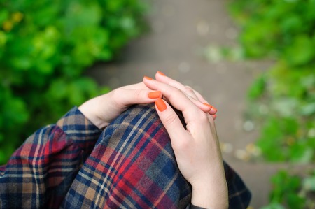 Girl with hands on lap. Women's hands with orange manicure. girl in a long checkered dress in a park...