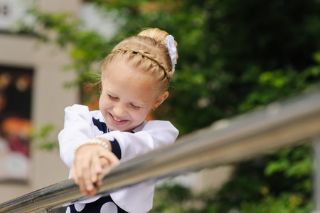 Portrait of a little girl. Child in a beautiful dress looking to side, hands on railing. Green tree in background. little girl laughsの写真素材