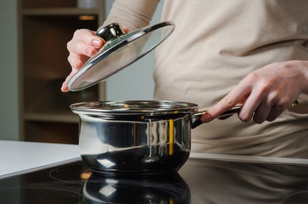 Female hand holding the lid of the pan. Person removing lid from cooking pot.の写真素材