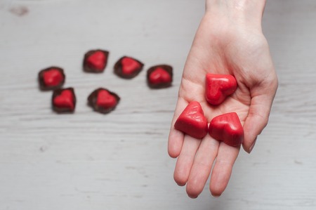 woman's hands full of chocolate sweets. Red chocolate hearts in hands on a white wooden background.