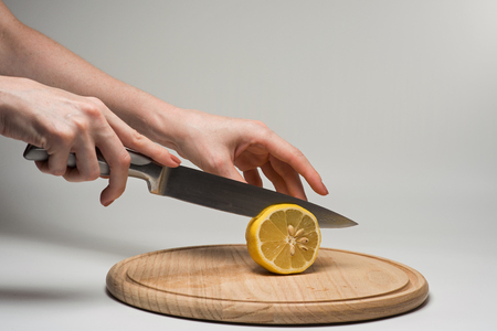 Girl cuts frash lemon into slices on a cutting board.の写真素材