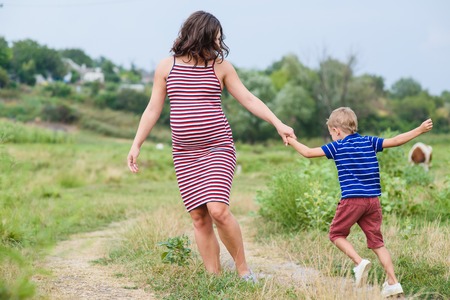 Pregnant woman walking countryside with her son.の写真素材