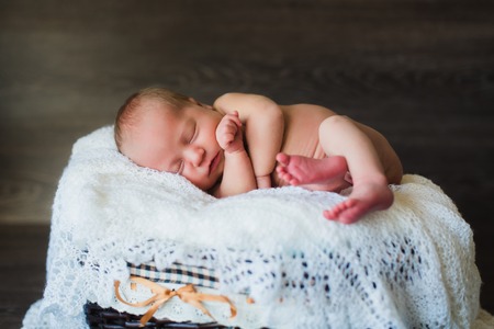 Adorable beautiful newborn baby girl. One week old newborn baby sleeping in basket. Dark wooden backgroundの写真素材