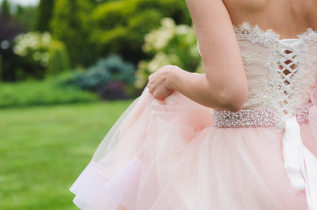 Close-up of a bride in a pink dress from the back. Woman stands with her back to the camera. Grass, trees and bushes in the background.の写真素材