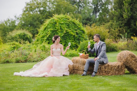 Bride and groom make toast sitting on a bale of hay. Grass, trees and bushes in the background.の写真素材