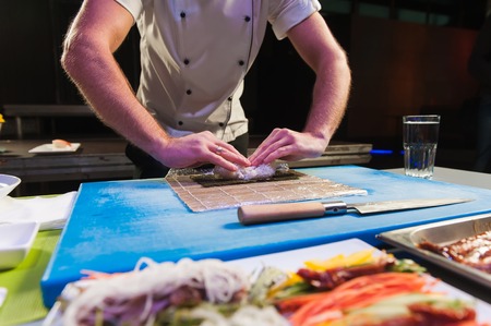 Male hands touch bamboo mat. Small mat on cooking board. Japanese chef at work. Man prepares sushi rolls.の写真素材