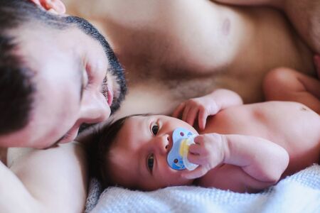 Happy father and a baby boy. Father and newborn lying on the bed. Child with a pacifier in his mouth. A man is hugging a child. View from aboveの写真素材