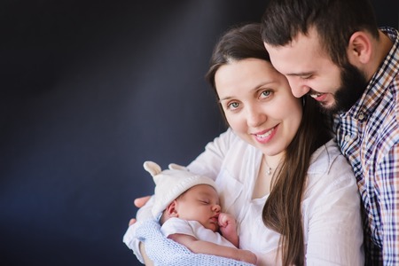 Portrait of happy parents with their newborn baby on a dark background.
