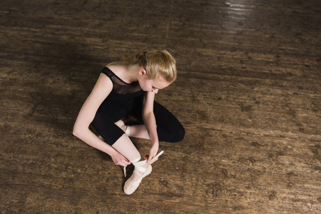 Young ballerina or dancer girl putting on her ballet shoes on the wooden floor. Top view.の写真素材
