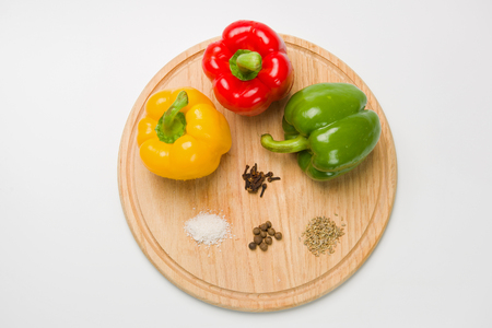 Three bulgarian peppers of different colors lie in a row on a wooden cutting board. Peppers with various spices. White background. View from above.の写真素材