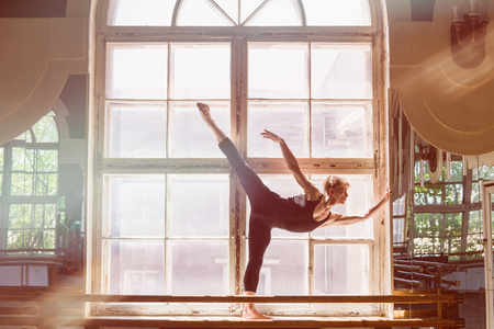Male ballet dancer is dancing in front of a large window, standing on the windowsill.の写真素材