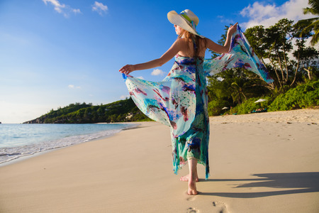 Back view of lonely girl with summer dress is walking along coastline.の写真素材