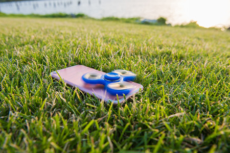Blue Tri Fidget Hand Spinner on the green grass. Spinner on the phone.の写真素材