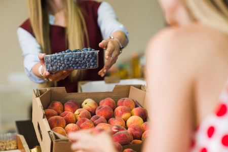 A woman buys berries in the market. Woman seller is holding blueberries in her hands. Focus on berries. Close-up.の写真素材