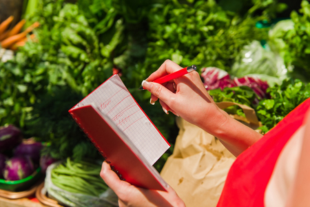 A woman crosses out purchases from shopping list. Girl with a notebook in hands.の写真素材