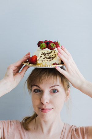 Happy lovely young woman holding birthday cake. Look at the camera. Gray background.の写真素材