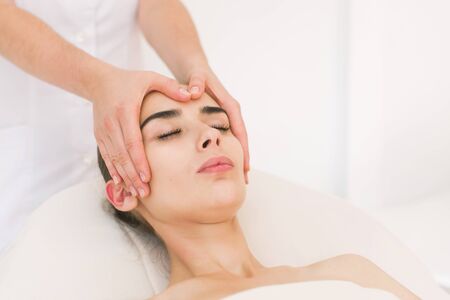 Facial massage beautiful girl. Portrait of a girl in a massage parlor. Beautician doing massage of female faces. Massage face girl close-up.の写真素材