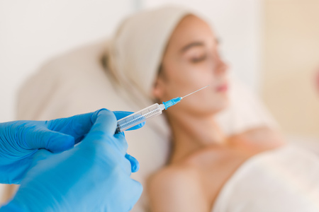 Close up view of doctor in sterile gloves making facial injection. Young pretty woman receiving treatments in beauty salons.の写真素材