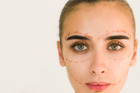 Beautiful girl with dark eyebrows with perforation lines on face, plastic surgery concept, close up...