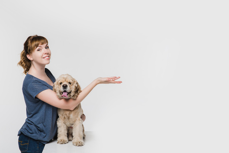 A woman with her American cocker spaniel pointing to space at right with hand isolated on white....