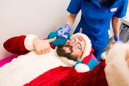 Spa facial mask application. Christmas man in Santa Claus clothes in beauty spa.の写真素材