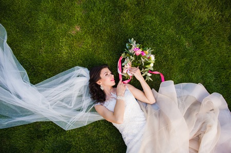 Beautiful brunette bride lying in the grassの写真素材
