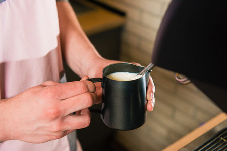 Hands holding cup with milk for coffee with machine. Barista with pitcher make milk foam.の写真素材