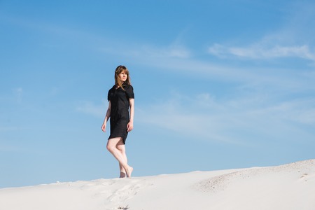 Young woman in black dress walk in sand dunesの写真素材