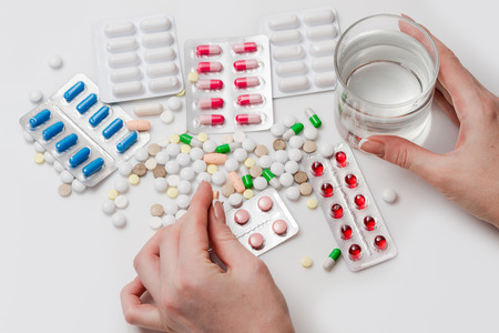 Pills with glass of water and hand holding pill.の写真素材