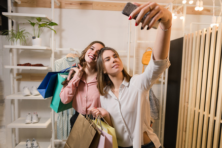 Happy girlfriends making selfie with shopping bags