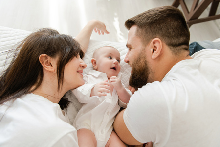 Happy smiling young family in bed with infantの写真素材