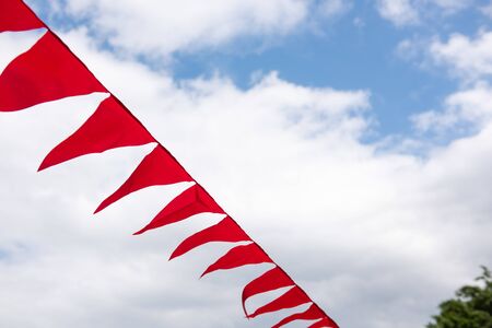 Red textile flags decoration line hanging up outdoors. Blu sky with clouds on background.の写真素材