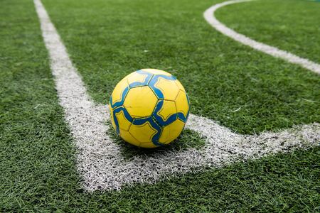 Soccer yellow ball with blue stripes on marked soccer football field corner.