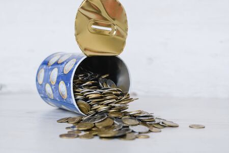 Last money in tin can close up, many silver and golden coins currency spread out on white tableの写真素材