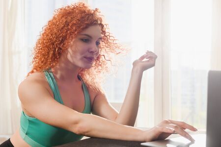 Young attractive woman wear sport clothes and look at laptop screen to start home sport training gym...