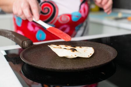 Woman hands hold silicone spatula, cook at kitchen tortillas, chapati, pita with dry ceramic pan on...