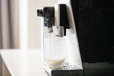 Hot milk foam pour flowing from coffee machine, capuccino maker filter holder close up, warm drink in glass cupの写真素材