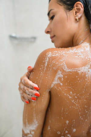Woman stay back in bathroom with wet skin, wash body and hair with shower gel at white background.
