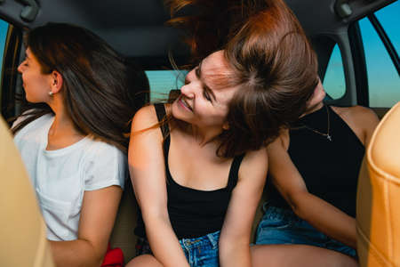 Three young female friends at car ride on back seat at salon, listen music, enjoy, dance, wave hair and going carefreeの写真素材