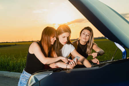 Three girls looking up information while trying to repair car engine.の写真素材