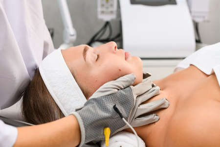 Hardware professional cosmetologist touch client face with gray microcurrent gloves for myostimulation skincare therapy close up, side viewの写真素材