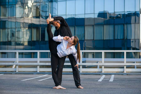 Flexible female make acro yoga element, stretching with male base partner while talk by mobile phone at urban background, sport and businessの写真素材