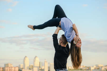 Base acroyoga partner hold female flyer up while she talk by mobile phone at sunset city background, sport and business conceptの写真素材