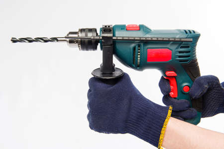 Male hands are holding an electric drill. Hands in blue gloves. Drill on a white background.の写真素材